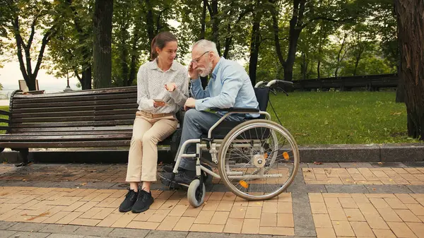 Genç bir kadın ve yaşlı bir adam parkta bankta oturmuş akıllı telefona bakıyor ve konuşuyorlar. Ortak ilgi ve bağlantı, nesiller arası boşlukları oluşturur.