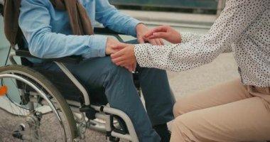 Tekerlekli sandalyedeki adam bankta oturan kadın bakıcının elini tutuyor. Destek ve bağlantı duygusu empati ve bakım kavramına odaklanır