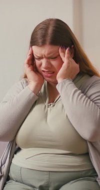 Şişman kadın, acı verici duygular gösteren parmaklarını şakaklarına bastırıyor. Yorgun kadın gözlerini kapatır. Düz bir şekilde oturmaktan rahatsız olduğunu gösterir.