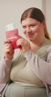 Gülümseyen ve beden ölçüsünde bir kadının elinde pasaport var. Bayan gezgin, yurtdışında satın alınma heyecanını göstermek için başparmağını kaldırdı.