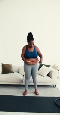 Ayrıca spor giyimli bir zenci kadın ölçüsünü bant ölçüsüyle ölçer. Eğitimden sonra oturma odasında kavisli kadın yoga minderinin yanında duruyor.