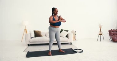 Artı boyut siyah kadın dizlerini büker vücudu derin çömelme pozuna sokar. Eller birbirine bastırarak dengeyi yaratırken kaslar güçlü bir hareketle geriliyor