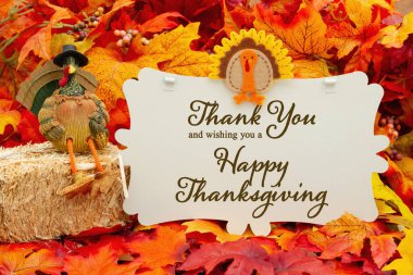 Happy Thanksgiving sign with a turkey on a bale of hay and fall leaves clipart