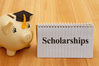 Scholarships message with gold piggy bank with a grad cap on wood desk for your money or saving for school