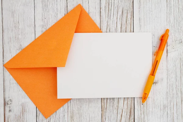 Blank greeting card with orange envelope and pen on weathered wood