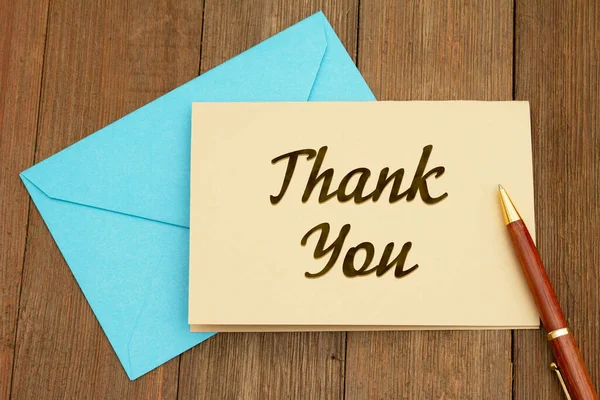 Thank you greeting card with blue envelope and pen on weathered wood