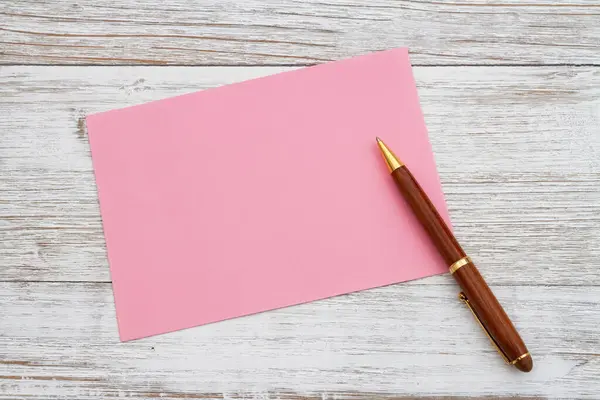 经风吹日晒的木头上有钢笔的空白粉红贺卡 图库图片