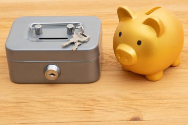 Saving and protecting your money with a gold piggy bank safety lockbox with keys on a wood desk clipart