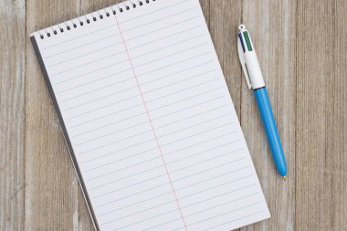 Boş bir sarmal defter ve yıpranmış tahta bir masa üzerinde bir kalem.