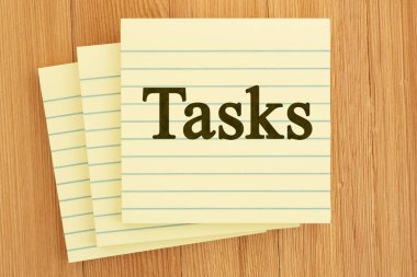 Ahşap bir masa üzerinde düzenleme ve planlama için gösterilen görev sözcüğü içeren sarı çizgili yapışkan notlar yığını