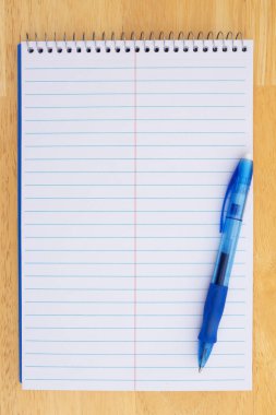 Mavi çizgileri ve ahşap bir yüzeye yerleştirilmiş mavi bir kalemi olan beyaz sarmal defter. Not almak, planlamak ya da yazmak için..