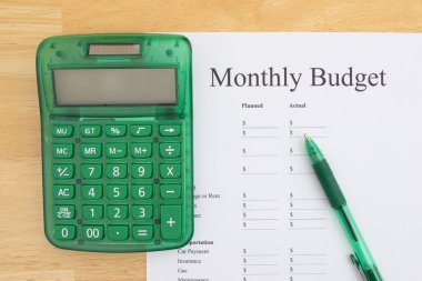 Yeşil hesap makinesi ve kalem, aylık bütçe kağıdının yanına, tahtadan bir masa üzerinde, finansal planlama için hazır..