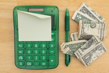 Yeşil hesap makinesi, yapışkan not, kalem ve ahşap bir masanın üzerine sarılı banknotlar, finans, bütçe ve para takibi için ideal..