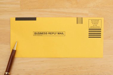 Üzerinde adres etiketi ve tahta yüzey üzerinde kalem olan iş iade zarfı. Posta ve yazışmalar için ideal.