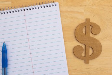 Ahşap bir masa yüzeyinde mavi bir kalem ve ahşap bir dolar işareti olan bir not defteri. Finans, bütçe ve tasarruf temaları için mükemmel.
