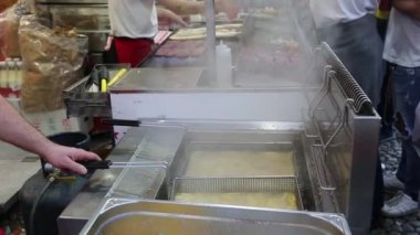 Sokak yemekleri satıcısı, kızarmış patatesleri dışarıda çıtır çıtır olana kadar sıcak yağda pişiriyor..