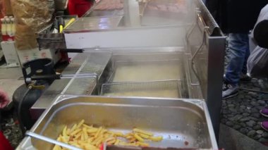 Sokak yemekleri satıcısı, kızarmış patatesleri dışarıda çıtır çıtır olana kadar sıcak yağda pişiriyor..