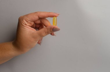 Gri arka planda iki yağ kapsülü tutan kadın. Refah kavramı. Yüksek kalite fotoğraf