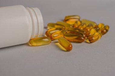 Omega-3 kapsülleri yeşil yapraklı arka planda beyaz bir şişede yatar. Balık yağı tabletleri. Biyolojik olarak aktif katkı maddeleri. Omega 6, Omega 9, A vitamini, E, D vitamini, D3 vitamini..