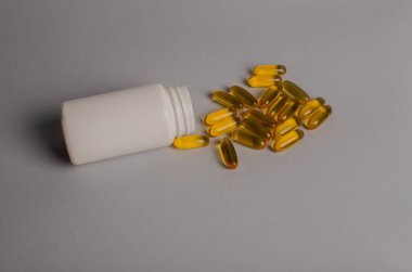 Omega-3 kapsülleri yeşil yapraklı arka planda beyaz bir şişede yatar. Balık yağı tabletleri. Biyolojik olarak aktif katkı maddeleri. Omega 6, Omega 9, A vitamini, E, D vitamini, D3 vitamini..