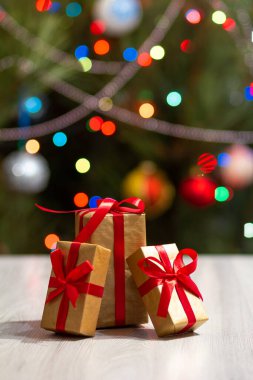 Kırmızı fiyonklu hediye kutuları. Arka planda parıldayan parti ışıkları ve oyuncak topları olan bir Noel ağacı. Noel kutlaması.