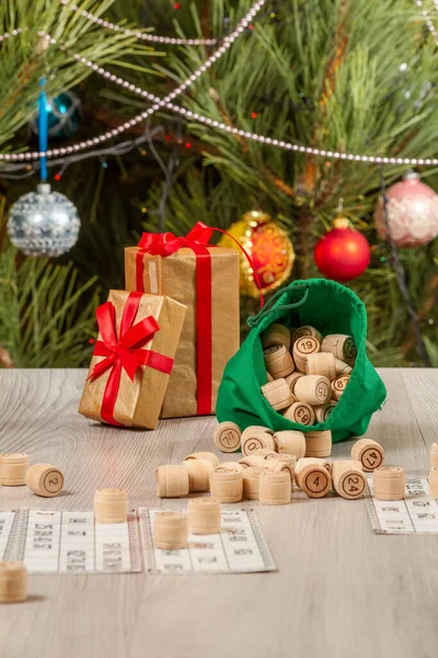 Board game lotto. Wooden lotto barrels with bag and game cards for a game in lotto. Gift boxes and Christmas fir tree with toy balls on the background.