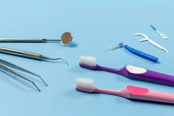 stock image Tweezers, a mouth mirror and a dental restoration instrument with toothbrushes, a silicone floss toothpick and interdental toothpick brushes on the blue background. Medical tools.