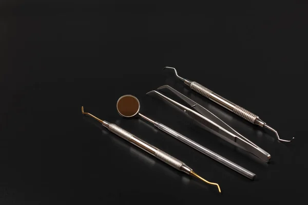 Set of metal instruments for dental treatment. Mouth mirror, tweezers, a dental restoration instrument and a curette on the black background. Medical tools.