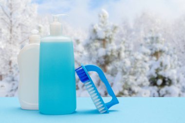 Plastik bulaşık deterjanı, cam temizleyici ve arka planda kış manzarası olan fırça. Yıkama ve temizlik konsepti.