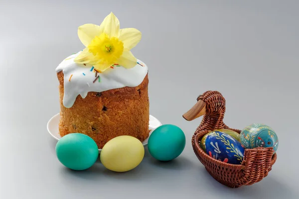 Sweet Easter cake with a daffodil flower and colorful Easter eggs in the wicker basket.