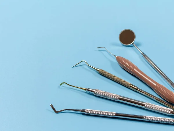 Mouth mirror, the dental restoration instrument, the curette and the plugger on the blue background. Medical tools.