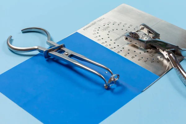 Dental hole punch, the metal plate, the rubber dam and the rubber dam forceps on the blue background. Medical tools concept.
