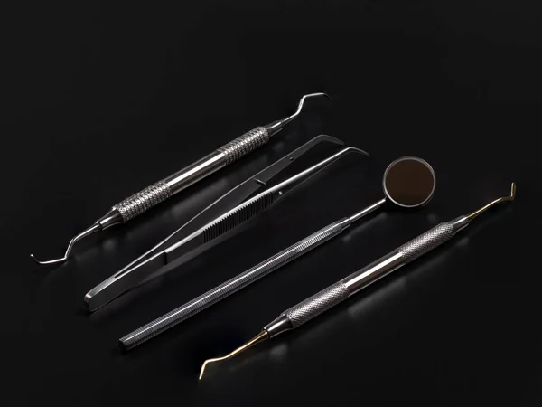 Set of metal instruments for dental treatment. Mouth mirror, tweezers, a dental restoration instrument and a curette on the black background. Medical tools. Top view.