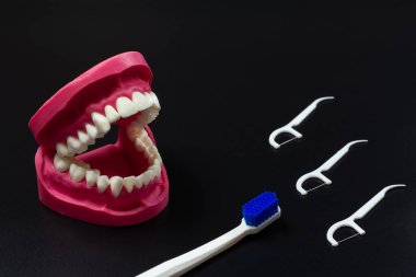 Siyah arkaplanda silikon diş ipi kürdanları ve diş fırçasıyla insan çenesi düzeni.