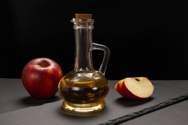Cam şişedeki elma sirkesi mantarlı, taze kırmızı bir elma ve siyah taş kesme tahtasına dilimlenmiş..