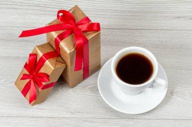 Bir fincan kahve ve gri arka planda kırmızı kurdeleli hediye kutuları. Üst görünüm.