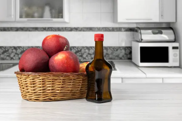 Apple vinegar in a glass bottle and fresh red apples in a wicker basket on the kitchen table. Organic food for health.