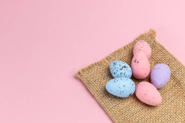 Çuval bezi ve pembe arka planda renkli Paskalya yumurtaları. Üst görünüm.