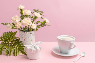 Vazoda sarı karanfiller, bir hediye kutusu ve pembe arka planda bir fincan kahve..