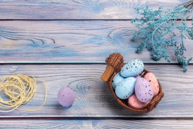 Hasır sepetteki renkli Paskalya yumurtaları, gemide bir ip ve dekorasyon bitkileri. Üst görünüm.