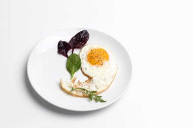 Beyaz arka planda kızarmış yumurta ve fesleğen yapraklı beyaz porselen tabak. Üst görünüm.