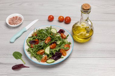 Taze domatesli salata, salatalık, roka, fesleğen, bıçaklı ıspanak. Zeytinyağlı bir şişe. Tuzlu kase. Sağlıklı sebze diyeti menüsü. Üst görünüm.