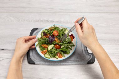 Taze domatesli salata, salatalık, roka, fesleğen, tabakta ıspanak. Çatallı kadın eli. Sağlıklı sebze diyeti menüsü. Üst görünüm.