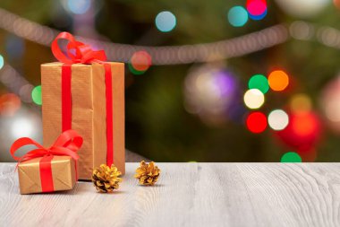 Noel süsü. Gri tahta tahtalarda kırmızı kurdele ve koni hediye kutuları ve arka planda şenlik ışıkları. Noel tebrik kartı konsepti.