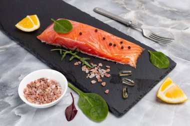 Çiğ somon balığı filetosu roka, fesleğen yaprağı, baharat ve dilimlenmiş limon. Mutfak masasında bir kase tuz ve çatal. Üst görünüm.