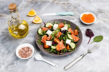 Dilimlenmiş somon balıklı salata, beyaz peynirli feta, taze domates, salatalık, roka, fesleğen, ıspanak. Kırmızı havyar ve tuzlu kase dilimlenmiş limon ve bir şişe yağ. Üst görünüm.