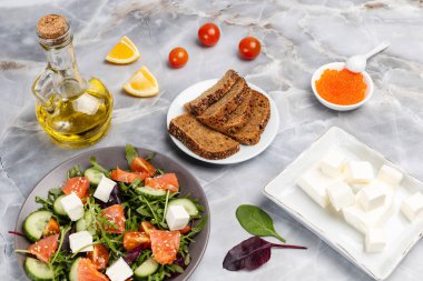 Dilimlenmiş somon balıklı salata, beyaz peynirli feta ve tabakta taze sebze. Kırmızı havyarlı kase, çavdar ekmekli bir tabak dilimlenmiş limon, bir şişe yağ ve peynirli bir tabak. Üst görünüm.