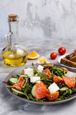Dilimlenmiş somon balıklı salata, beyaz peynirli feta ve tabakta taze sebze. Bir tabak çavdar ekmeği, bir şişe yağ, taze domates ve mutfak masasında dilimlenmiş limon..