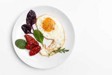 Karabiberli sahanda yumurta, susam, kurutulmuş domates, roka ve beyaz tabakta fesleğen. Üst görünüm.