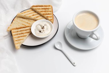 Kahvaltı için peynirli tost, beyaz porselen bir fincan sade kahve ve beyaz arka planda bir kaşık. Üst görünüm.